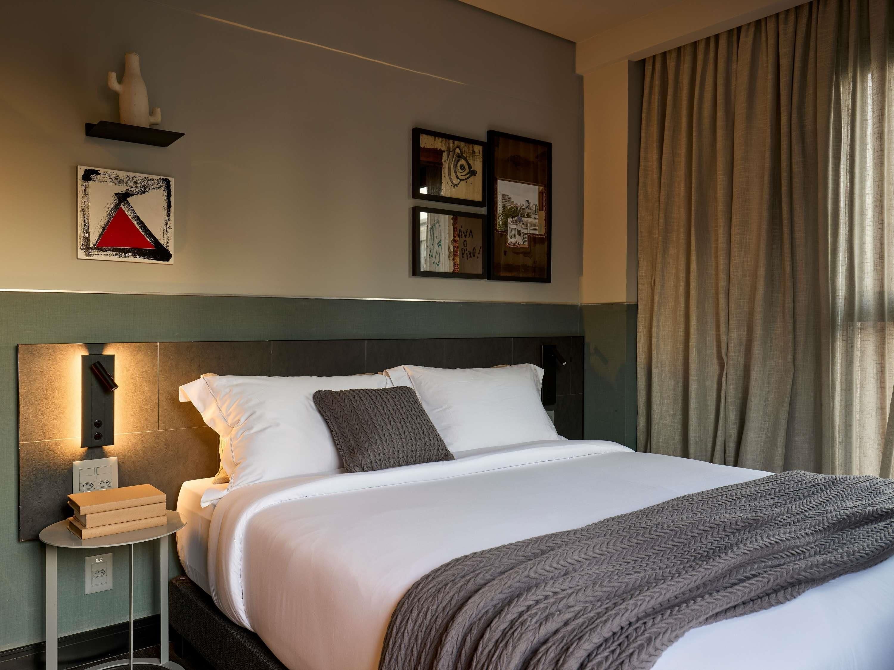 Habitació d'hotel amb un llit, una taula de nit, una làmpada penjada a la paret i obra d'art.