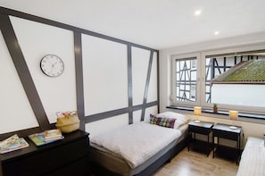 A bedroom with a bed, bedside tables, a clock, a window with a view, and a small plant on the windowsill.