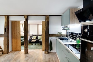 A modern kitchen with wooden beams, a built-in stove, and a view to a living area with a sofa.
