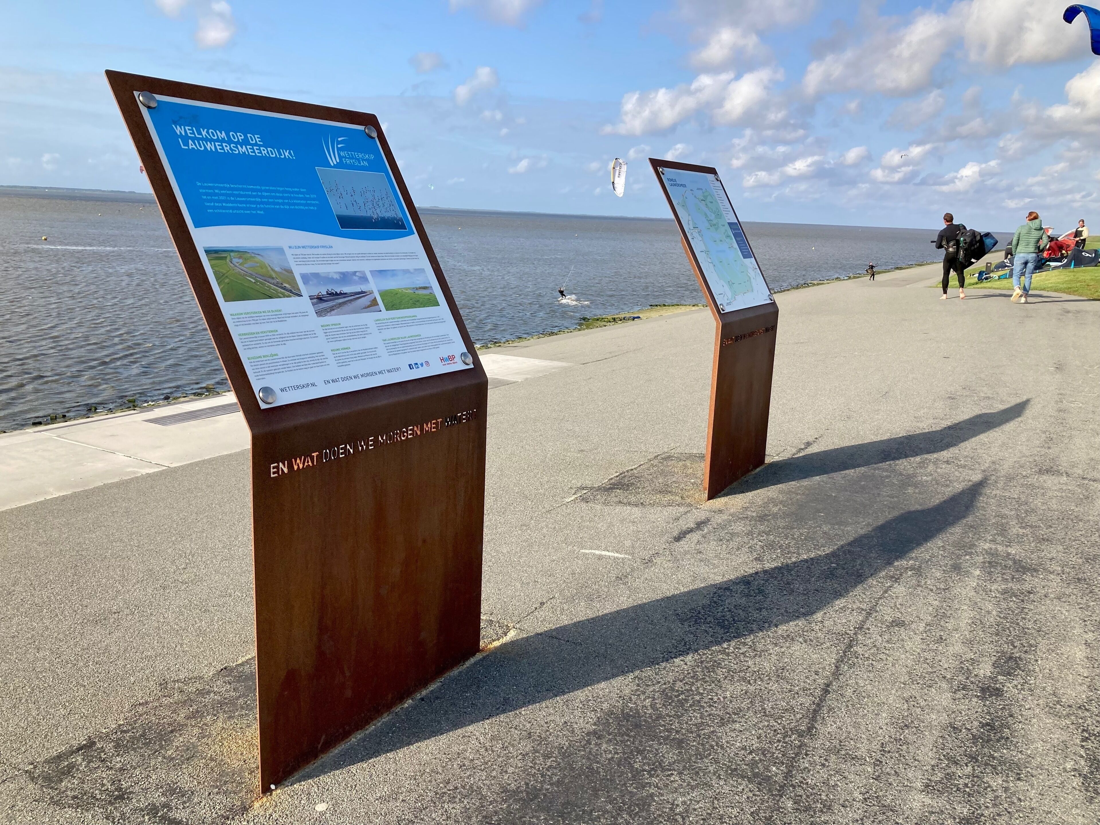 Two informational signs by a waterfront, one displaying a welcome message and the other a map.