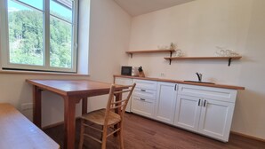 A kitchen with a wooden table, a chair, white cabinets, and a window with a view of trees. - Vila Zora | Studio apartment | Jezersko (Zgornje Jezersko)