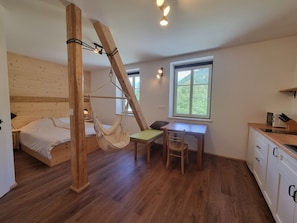 A room with a bed, a hammock, a desk, and a window.