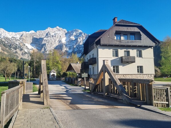 A mountain-view hotel with a wooden deck, stone walls, and a mountain backdrop.