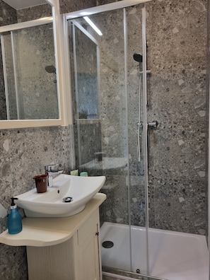 A bathroom with a glass-enclosed shower, a white sink, and a marble-tiled wall.