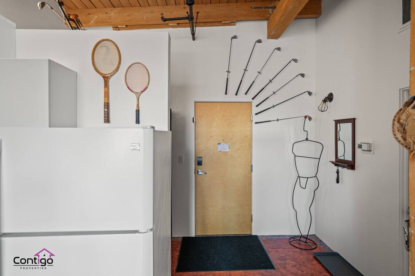 A hallway with a white refrigerator, wooden ceiling beams, a wooden door, and a wall-mounted towel rack.