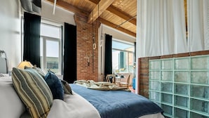 A bedroom with a bed, a brick wall, a window, and a view of the outside.