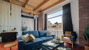 A modern living room with a blue sofa, a wooden coffee table, and a brick wall.