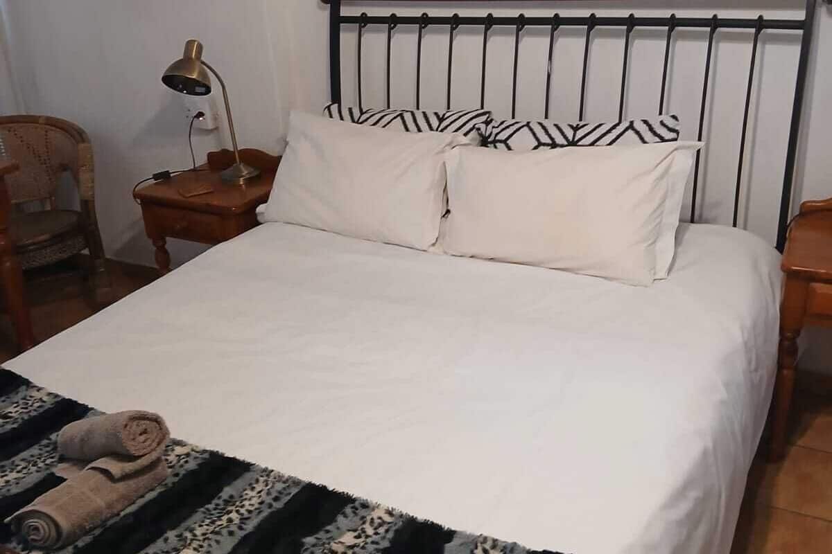 A bedroom with a bed, a nightstand, a lamp, a chair, and three framed pictures on the wall.