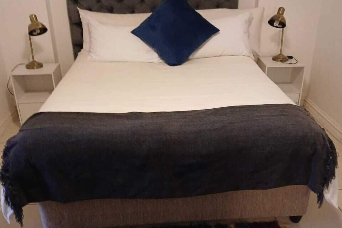 A bed with a tufted headboard, white bedding, a blue pillow, and a striped rug.