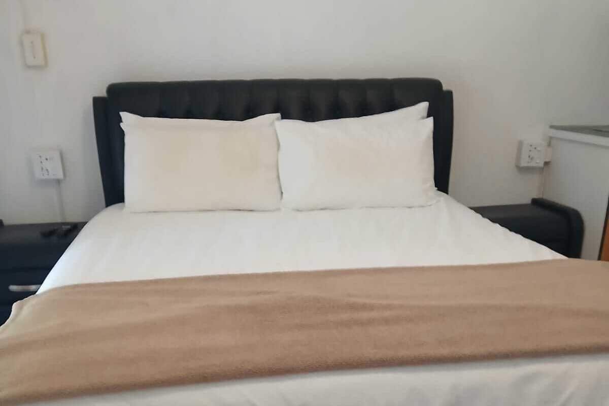A bed with a black headboard, white bedding, and a brown throw blanket.