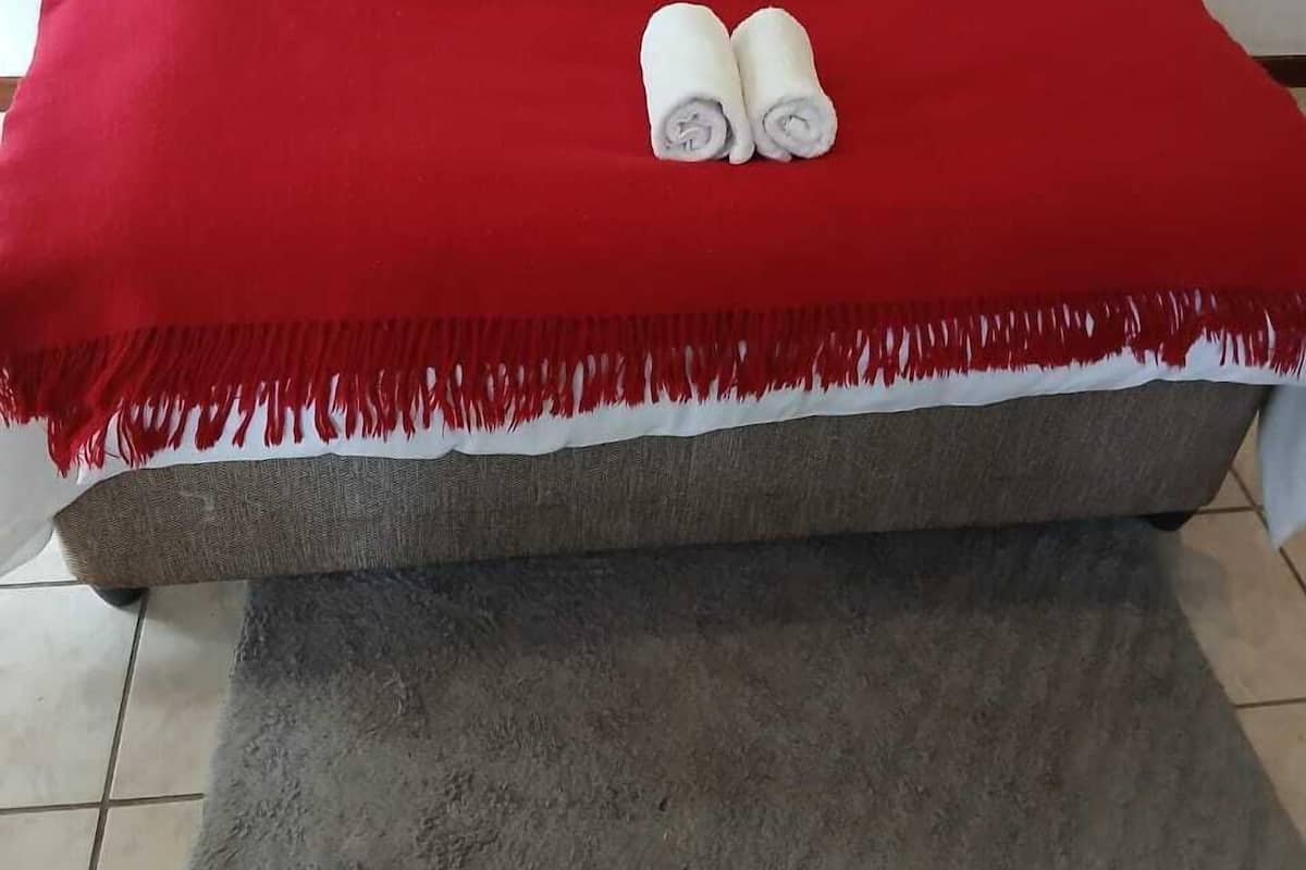 A neatly made bed with white linens, a red blanket, and two rolled towels.