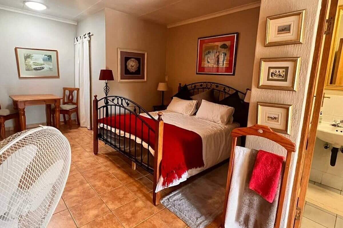 A bedroom with a bed, a chair, a table, and a hanging towel rack.
