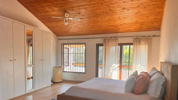 A bedroom with a wooden ceiling, a bed with pillows, a radiator, and a window with curtains. - Oaktree Guest House (Sandton)
