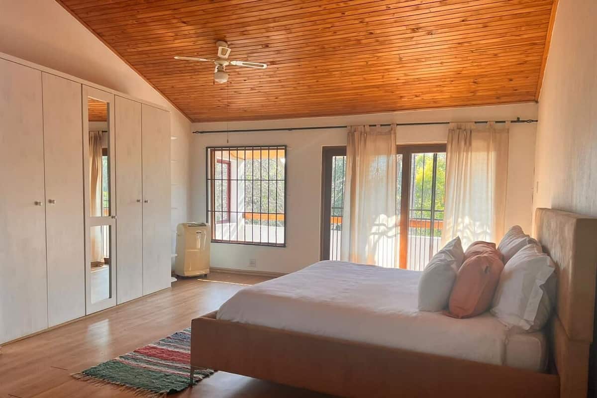 A bedroom with a wooden ceiling, a bed with pillows, a radiator, and a window with curtains.