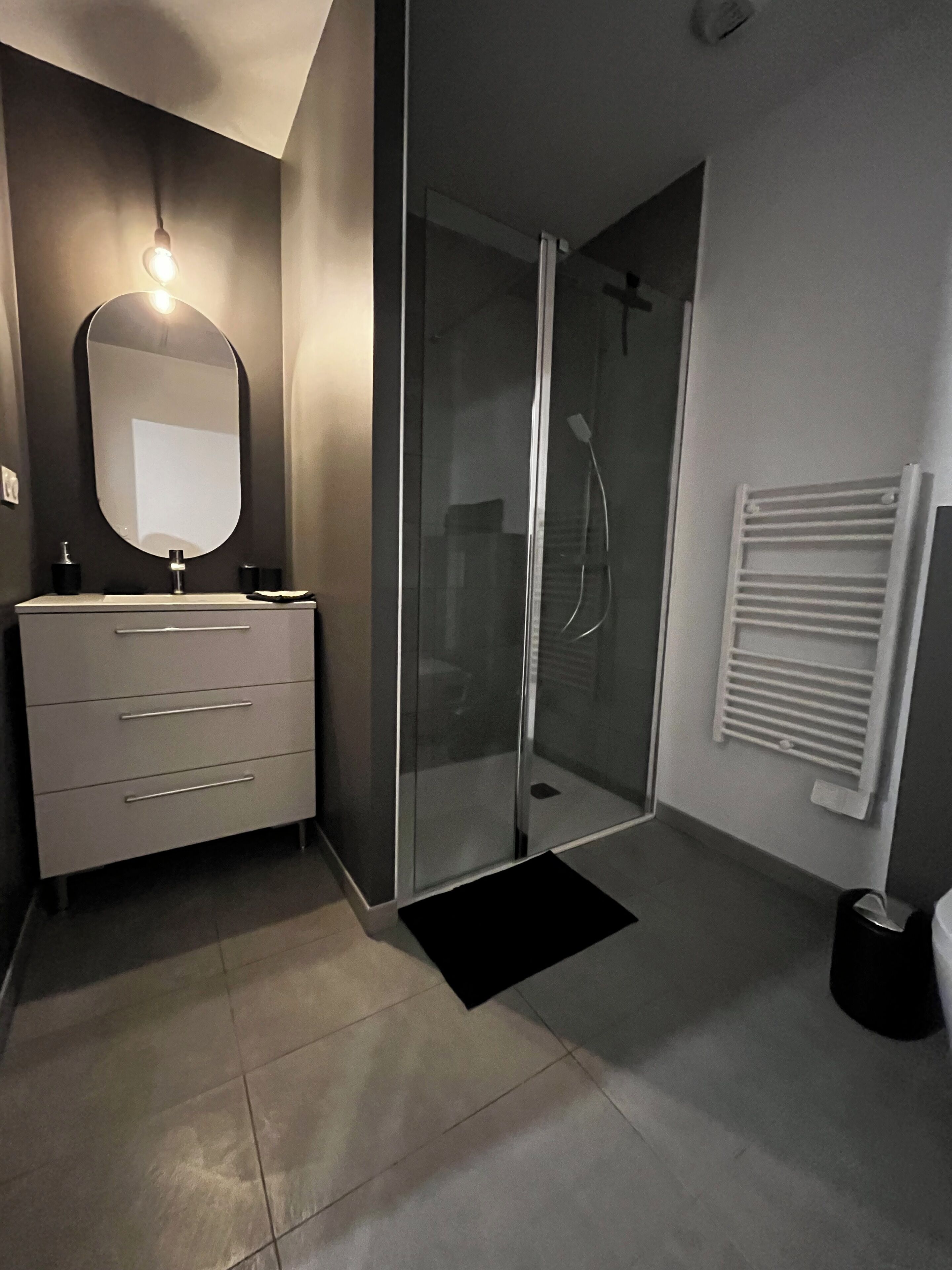 Een moderne badkamer met een glazen douchecabine, een wit wastafelmeubel met een spiegel en een handdoekrek.