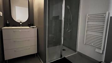 Een moderne badkamer met een glazen douchecabine, een wit wastafelmeubel met een spiegel en een handdoekrek.