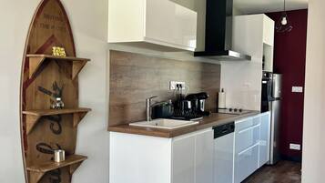 Een moderne keuken met witte kasten, een houten spatwand en een geïntegreerd eiland met een spoelbak. Op de muur bevindt zich een houten plank met decoratieve objecten, en een hanglamp hangt boven het eiland.