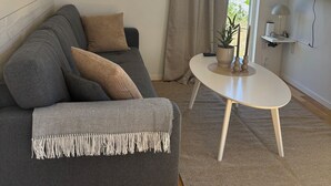 A modern living room with a grey sofa, a round mirror, a television, and a small table with a plant.