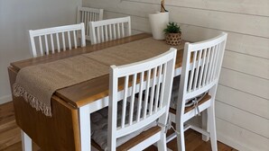 A dining area with a wooden table and white chairs, a pendant light, and a framed artwork on the wall.