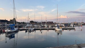 A marina with various boats docked, calm water, and buildings in the background.