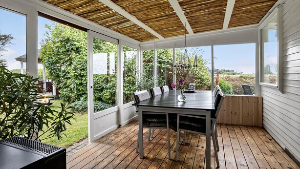 A covered patio with a wooden table and chairs, large windows, and a hanging light fixture. - Amazing home in Otterup with house sea view (Otterup)