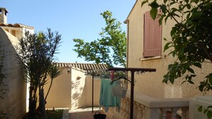 A courtyard with a pergola, a stone pathway, and a building with a tiled roof and shutters. - Herault coquet F2 Maraussan 34370 (Maraussan)