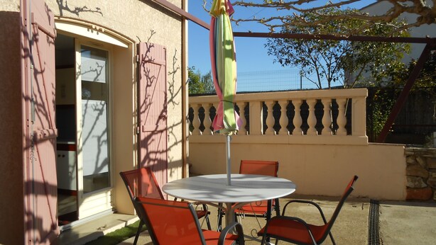 An outdoor patio with a round table and two chairs, a partially open door, and a balcony with a railing. - Herault coquet F2 Maraussan 34370 (Maraussan)
