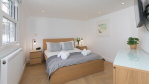 Une chambre moderne avec un lit en bois, des murs blancs, un radiateur, une table de chevet avec une lampe et un téléviseur fixé au mur.