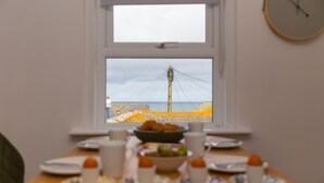 Une table de petit-déjeuner avec des assiettes, des tasses et un saladier de fruits, placée devant une fenêtre donnant sur une plage et des lignes électriques.