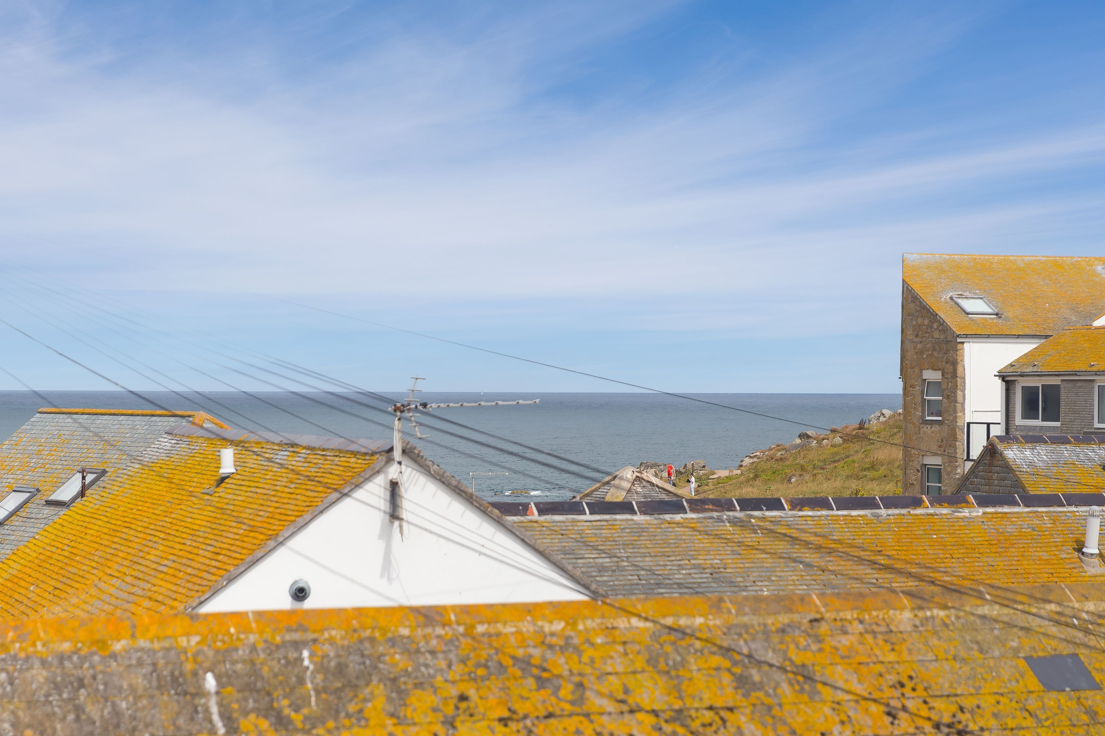 Ein Küstengebäude mit mehreren gelb-gefliesten Dächern, einem weißen Abschnitt und Blick aufs Meer.