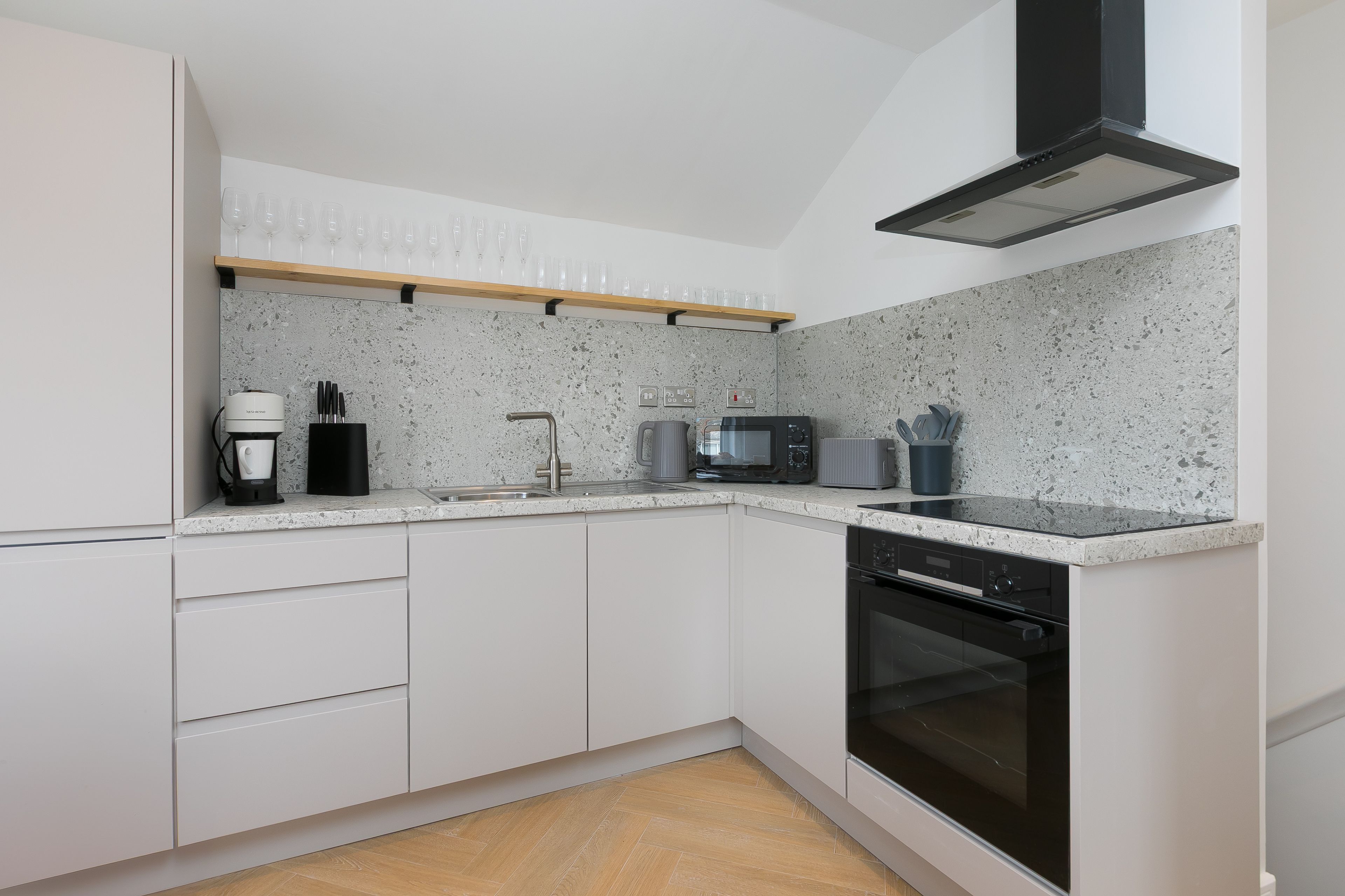 A modern kitchen with white cabinets, a granite countertop, a built-in oven, a microwave, a coffee maker, and a wine rack.