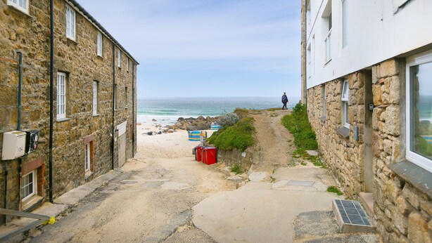Un étroit sentier de pierres menant à une plage, sur lequel on voit une personne s’éloigner de la caméra.