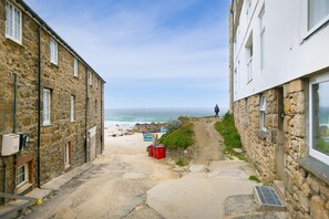 Un étroit sentier de pierres menant à une plage, sur lequel on voit une personne s’éloigner de la caméra.