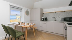Une cuisine moderne avec des meubles blancs, une table à manger en bois et une vue sur la mer par la fenêtre.