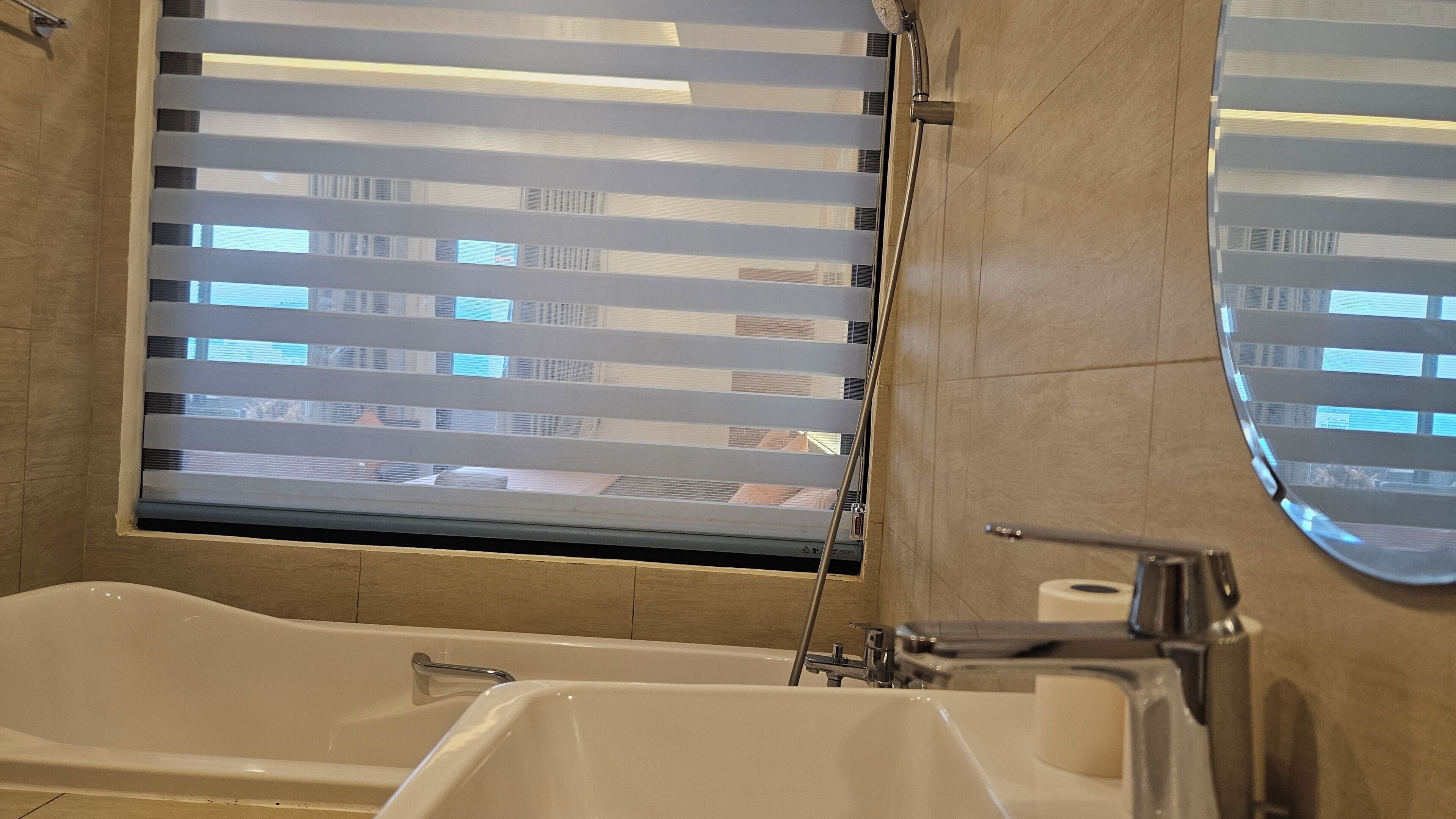 Un baño con bañera, inodoro, espejo y ventana con persianas.