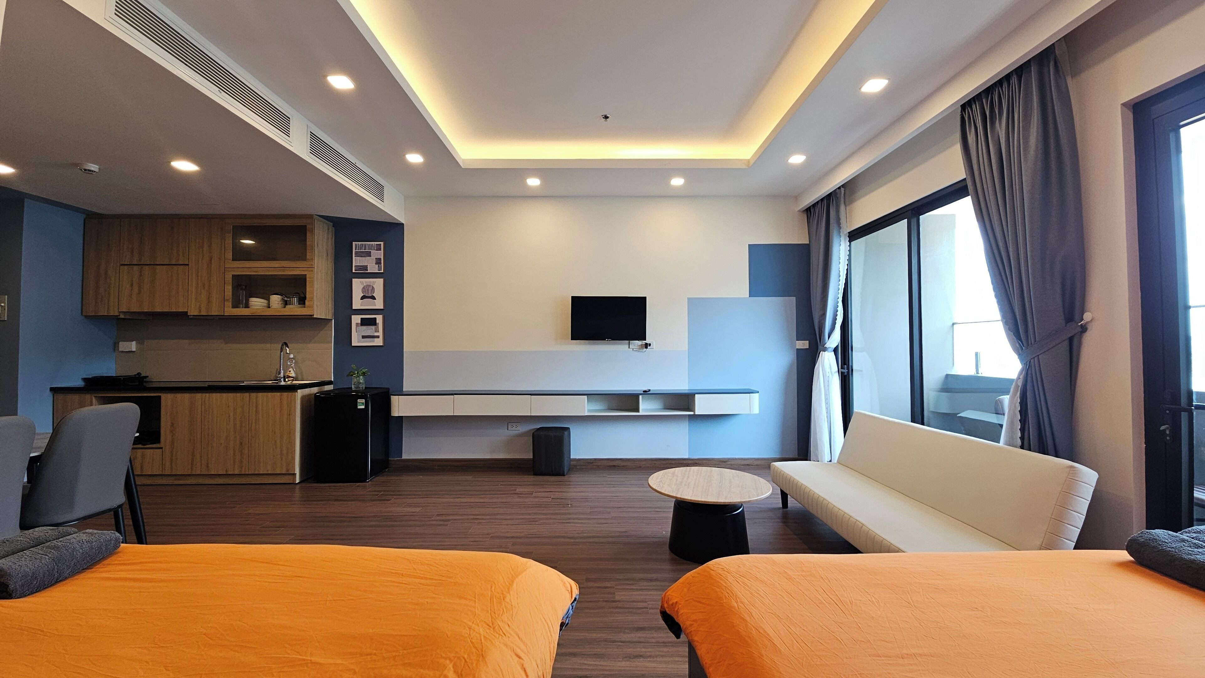 Una habitación de hotel moderna con kitchenette, un televisor en la pared, un sofá y dos camas.