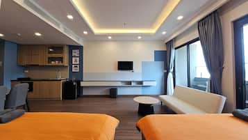 Una habitación de hotel moderna con kitchenette, un televisor en la pared, un sofá y dos camas.