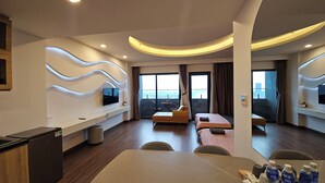 Een moderne hotelkamer met een flatscreen televisie, een bank, een eettafel en een balkon met uitzicht.