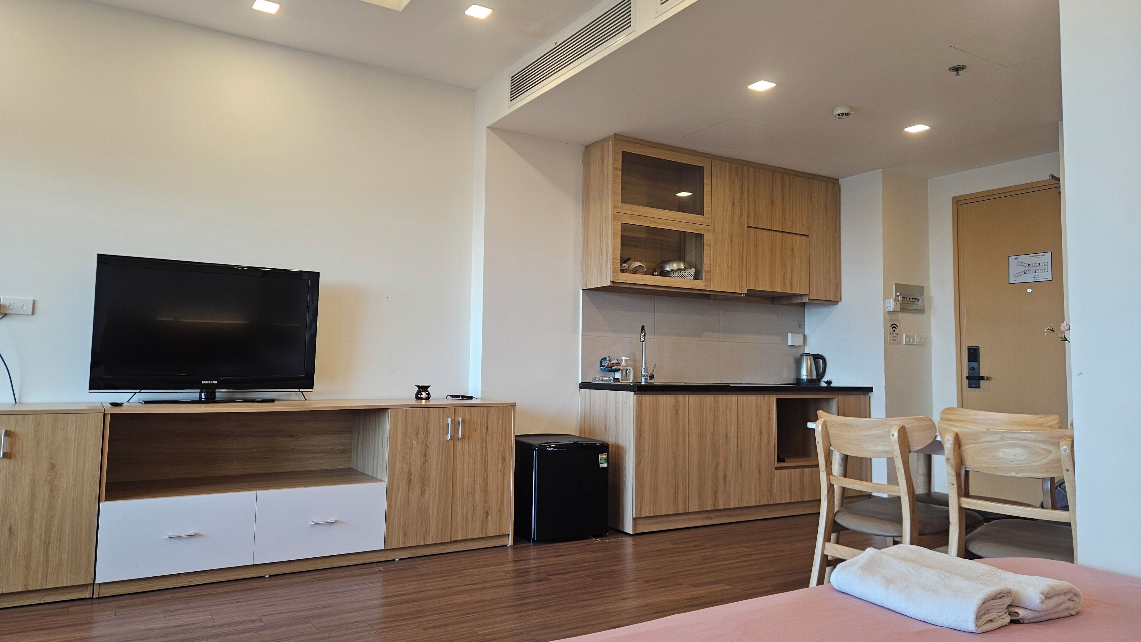A modern kitchen with wooden cabinets, a black refrigerator, and a flat-screen TV.
