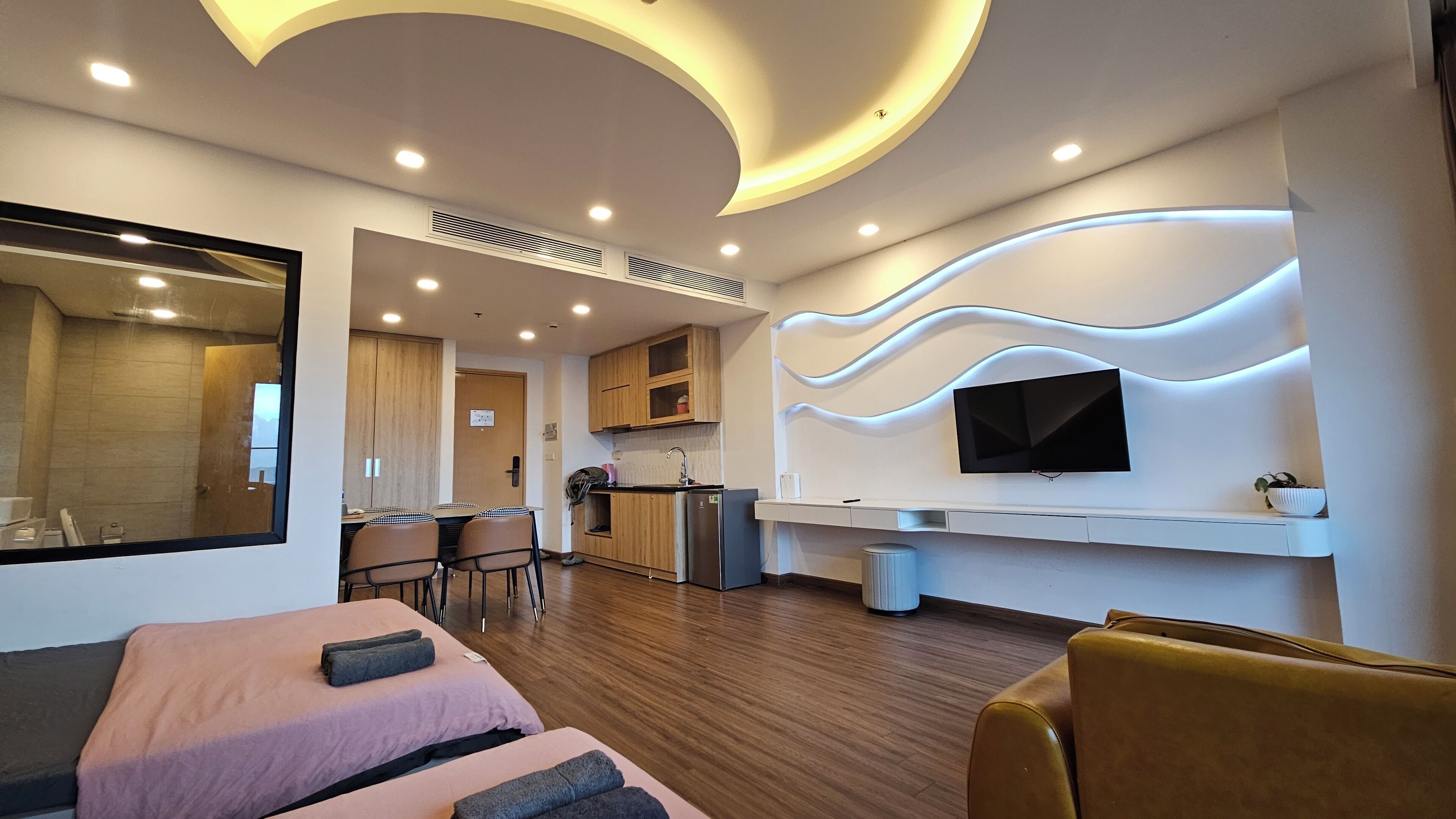 Una moderna camera d'albergo con pavimento in legno, un divano, una TV a parete e un angolo cottura con mobili in legno.