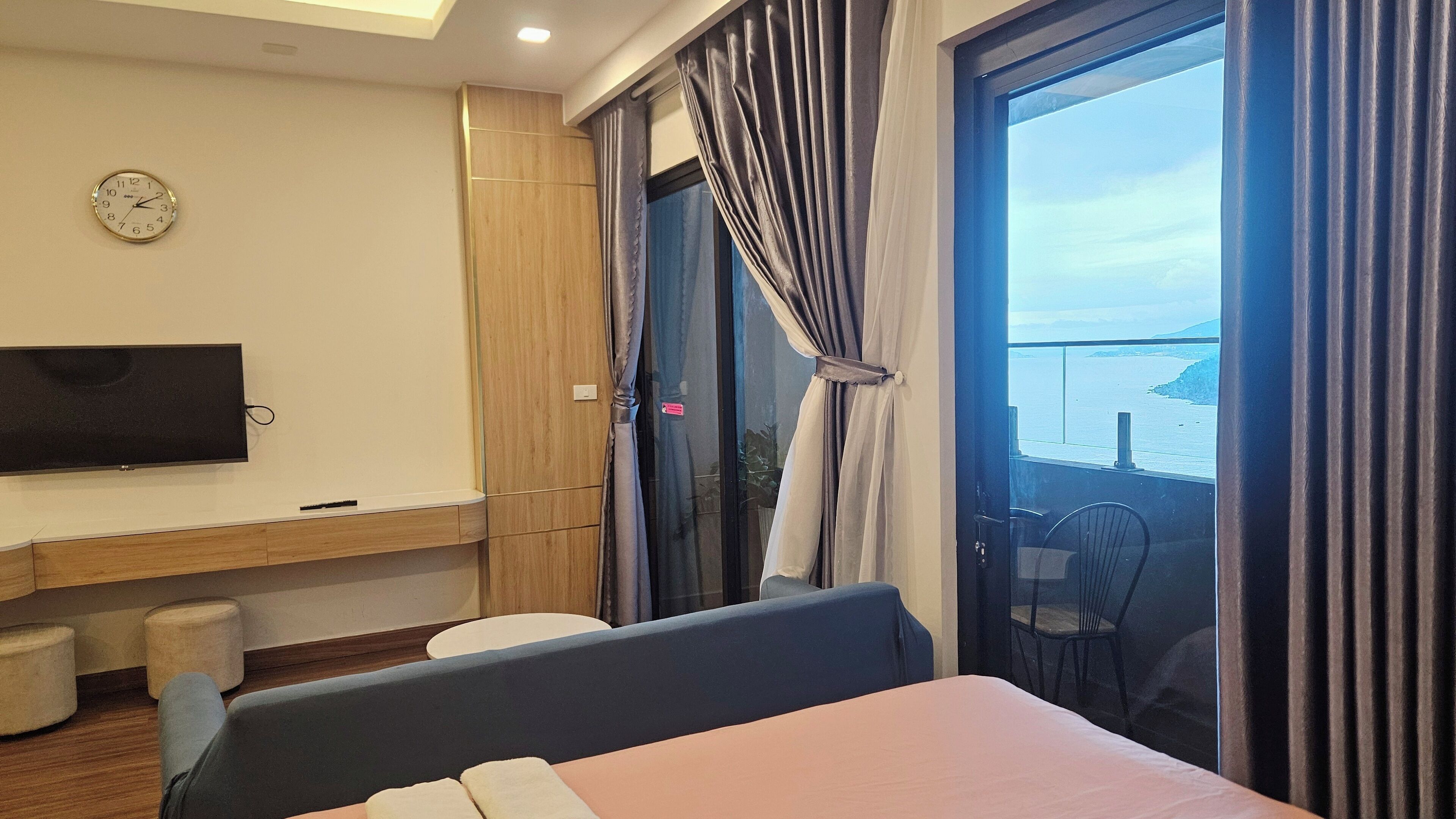 A modern hotel room with a bed, a TV, a balcony with curtains, and a view of the sea.
