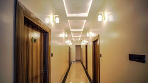 A hotel hallway with wooden doors, a marble floor, and recessed lighting. - Aryavarta Hotel (Faizabad)