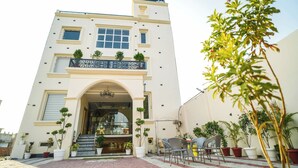 A two-story building with a balcony, potted plants, and outdoor seating. - Aryavarta Hotel (Faizabad)