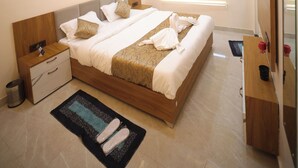 A modern hotel room with a large bed, bedside tables, a small desk, and a ceiling fan. - Aryavarta Hotel (Faizabad)