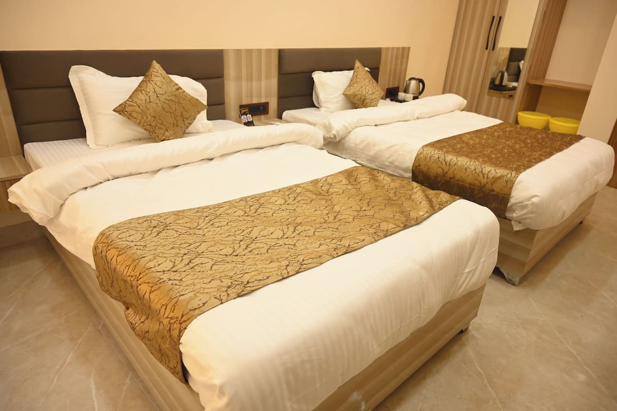 Habitación de hotel con dos camas, cada una con ropa blanca y una manta dorada estampada.