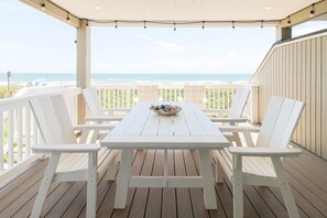 A covered outdoor seating area with a table and chairs, overlooking the ocean.