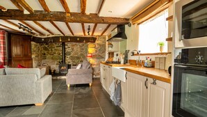 A cozy kitchen with a stone wall, wooden beams, a grey sofa, and a modern stove. - Penclogwynau (Dolgellau)
