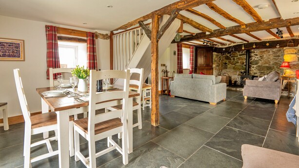 A spacious living area with a dining table set for four, a staircase, and a stone fireplace. - Penclogwynau (Dolgellau)