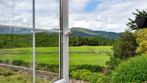 A view through a window of a green landscape with stone walls and a distant mountain range. - Penclogwynau (Dolgellau)