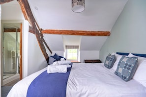 A bedroom with a large bed, a wooden ceiling beam, a window with blinds, and a glass shower enclosure. - Penclogwynau (Dolgellau)